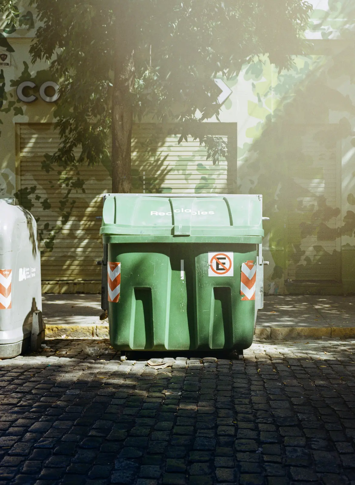 A green recycling container standing on cobbles