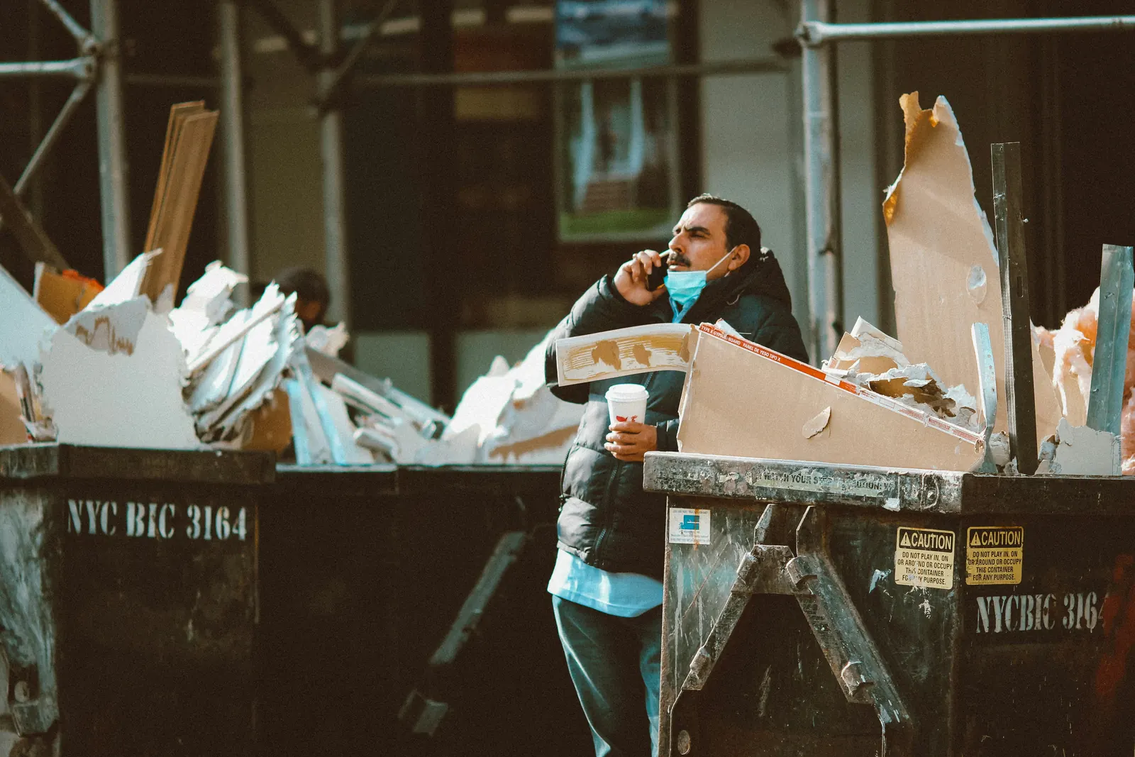 A worker on the phone beside a dumpster of drywall